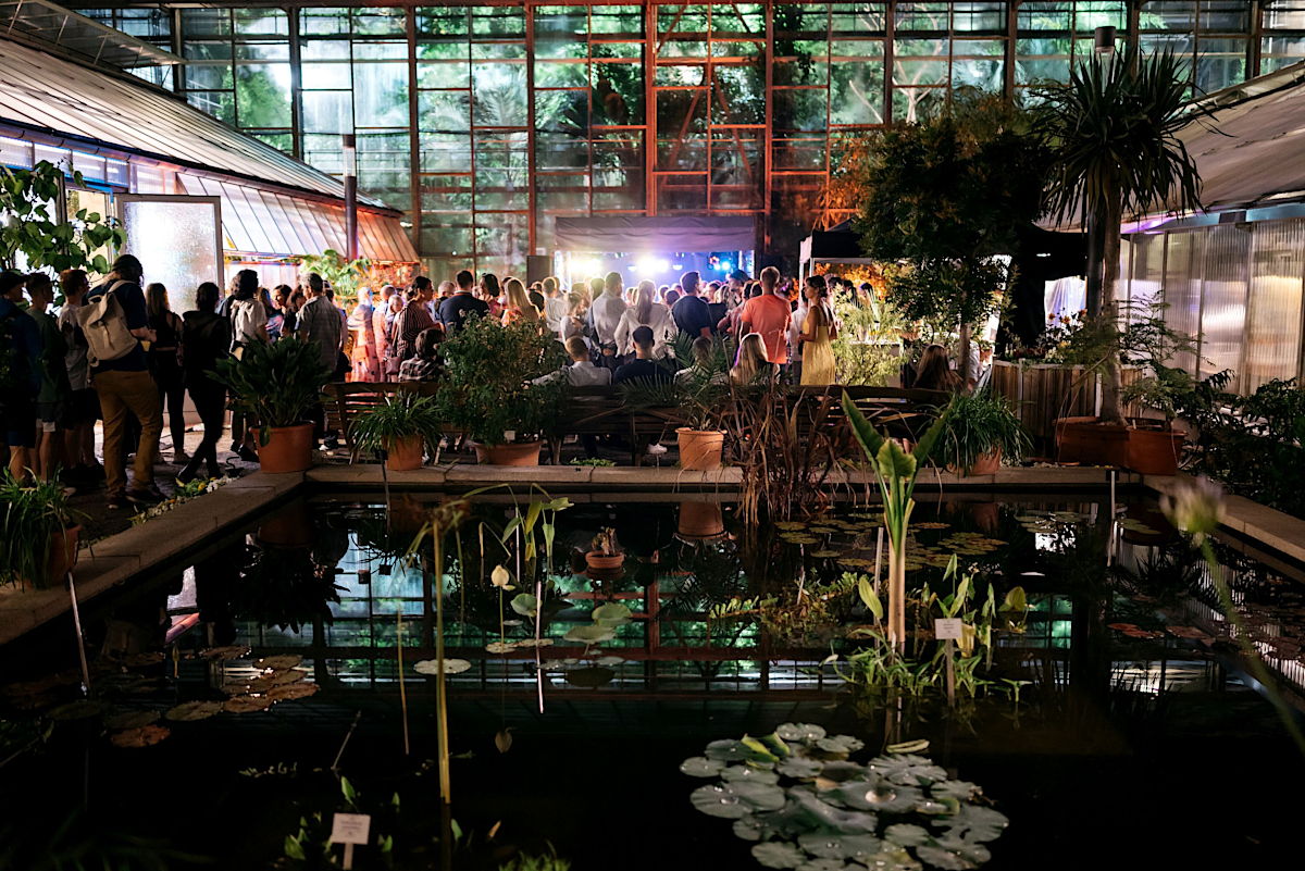 Universitätssommerfest 2022 am Schillertag 2022, den 24.6.2022, im Botanischen Garten der Friedrich-Schiller-Universität Jena in Jena. Teich und Bühne im Innenhof des Botanischen Gartens. Besucher genießen zahlreich die Musik vor dem großen Gewächshaus. Foto: Christoph Worsch/Universität Jena